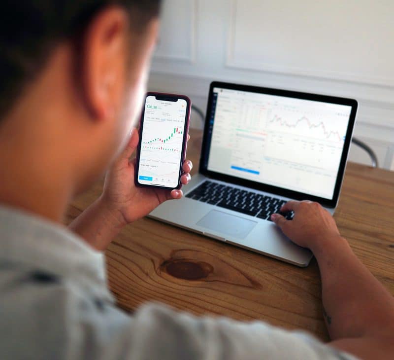 Man on Computer and Phone Looking at Stocks