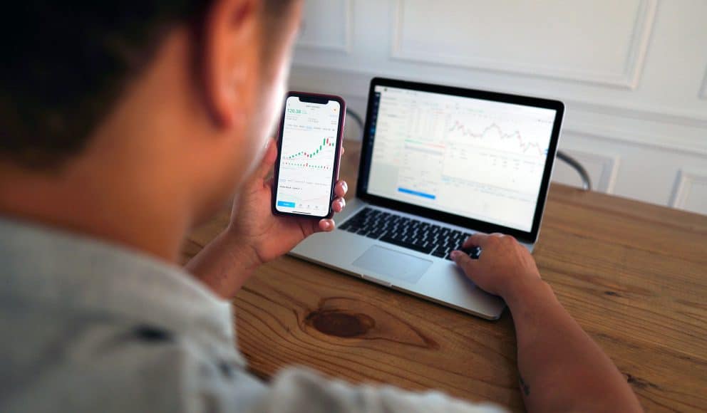 Man on Computer and Phone Looking at Stocks